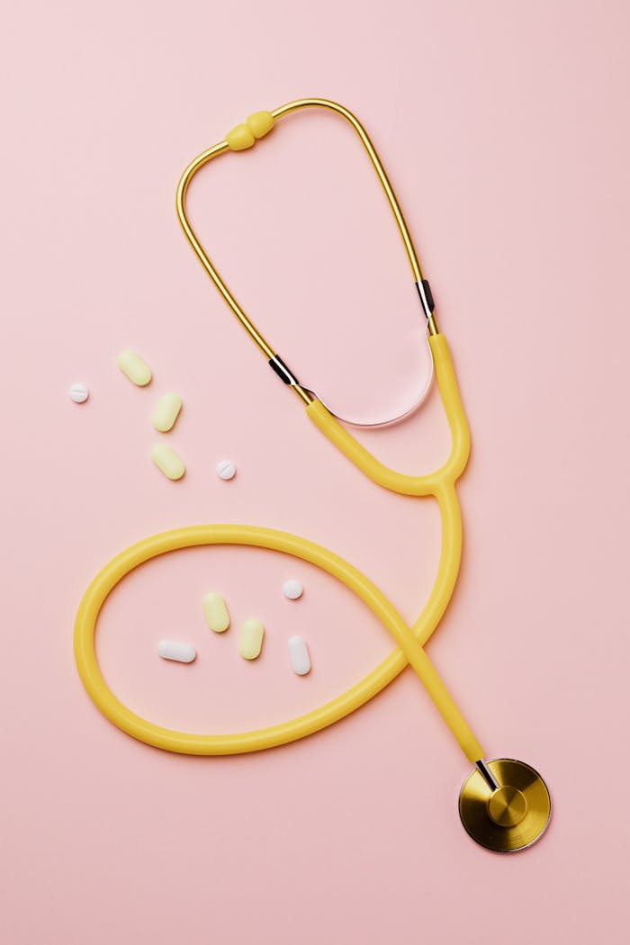 services-01 Flat lay of a yellow stethoscope and assorted pills on a pastel pink background.