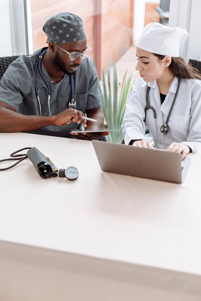 services-04 Two doctors discussing patient care with devices on a glass table indoors.